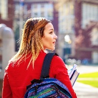 woman walking on college campus holding books and carrying backpack