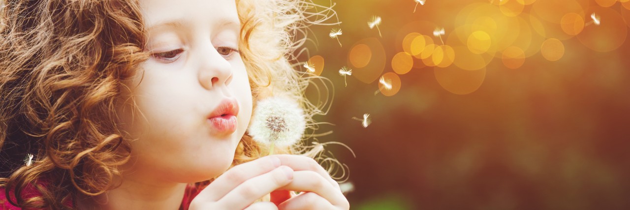 Getting an Autism Diagnosis Meant Emotional Support for My Kid Little curly girl blowing dandelion.