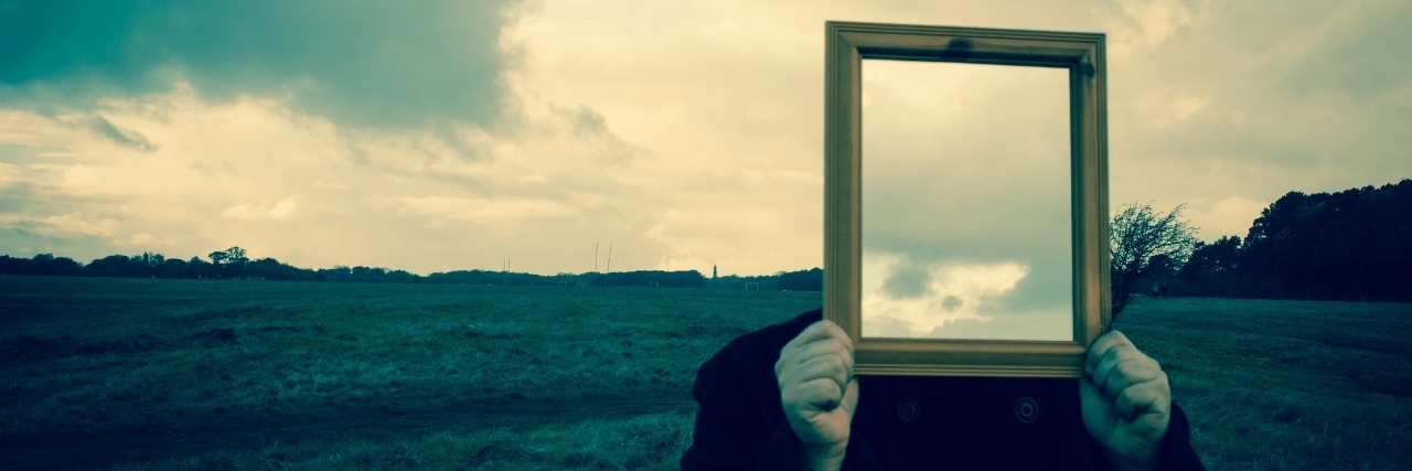 Man with mirror in front of face, reflecting sky