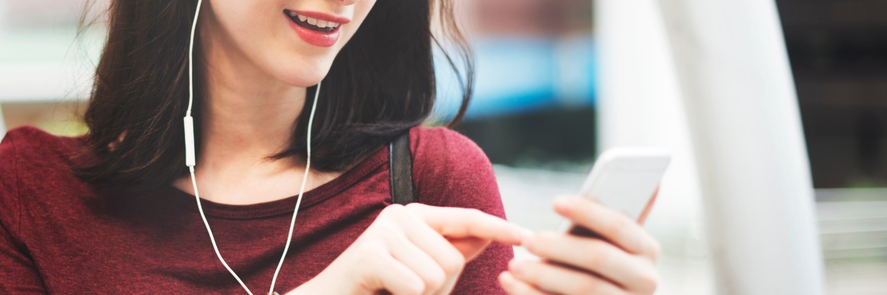 Cystic Fibrosis: Playlist of Songs for People With Health Challenges woman with dark hair in red shirt walking outside and listening to music on her phone