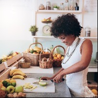 Shot of young african woman working at juice bar and cutting fruits. Female bartender making fresh juice.