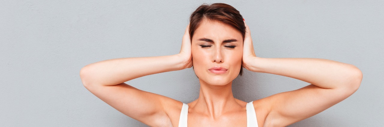 Depression: When People Compare Your Struggles to Others' a young woman covering her ears with her hands with her eyes closed