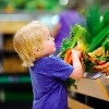 young boy in supermarket grabbing carrots off a produce shelf