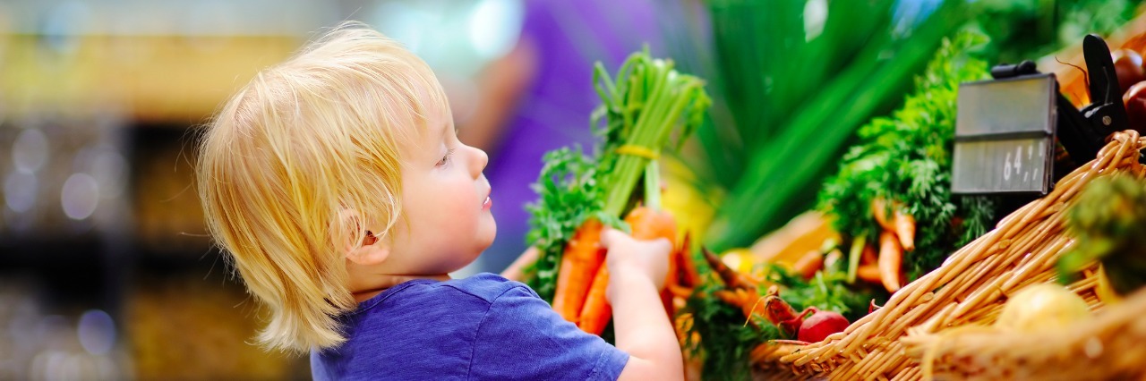 Autism: How Building a Village Has Helped Support Our Son young boy in supermarket grabbing carrots off a produce shelf