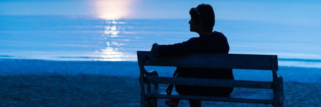 Woman sitting on bench at the beach at night