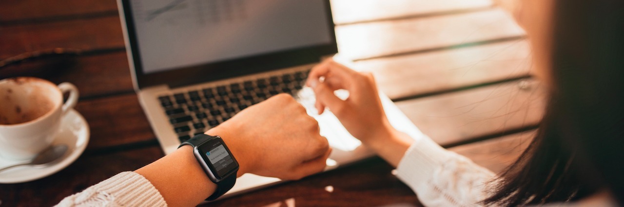 Woman sitting at her computer, looking at her watch