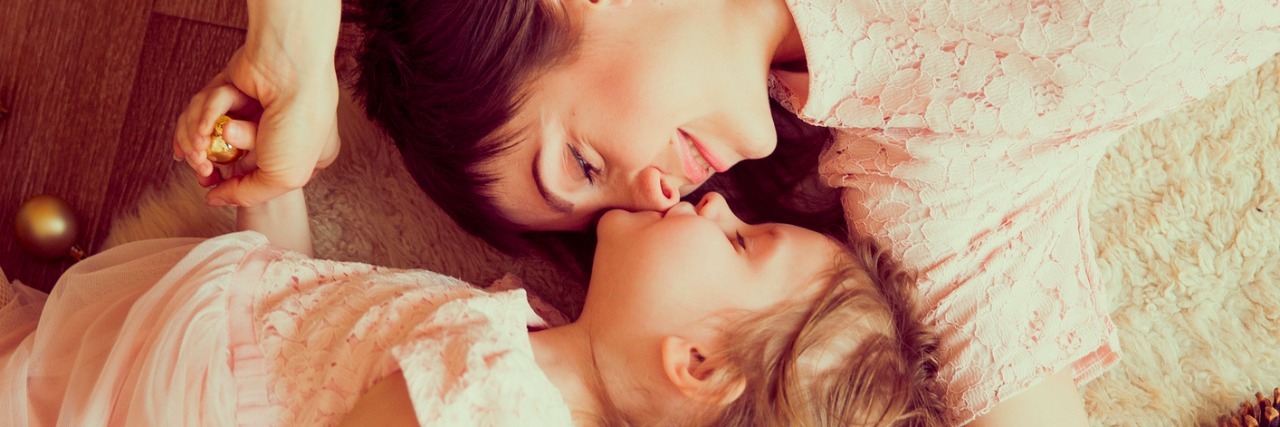 mother and daughter lying together on carpet near christmas decorations