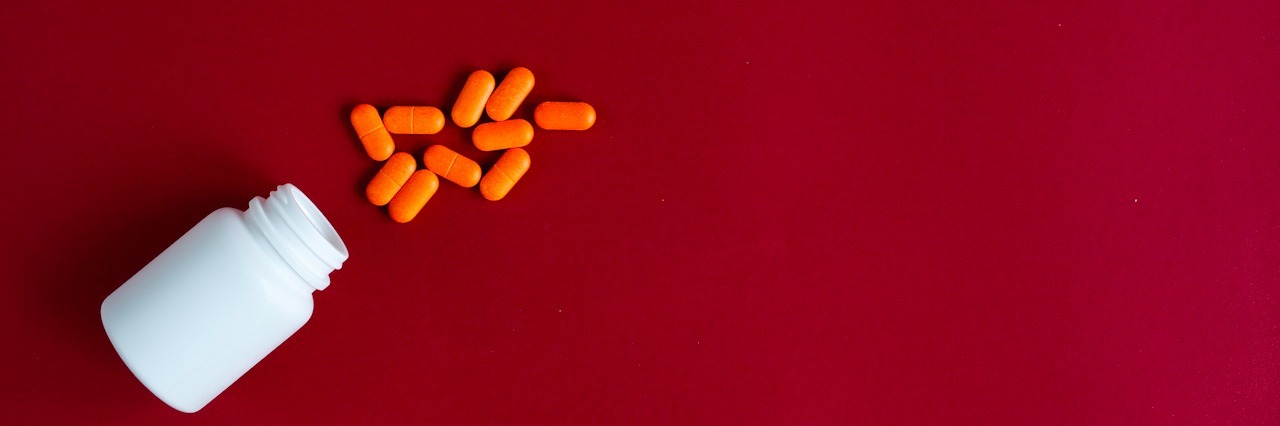 orange tablets in plastic container on red background top view