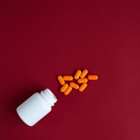 orange tablets in plastic container on red background top view