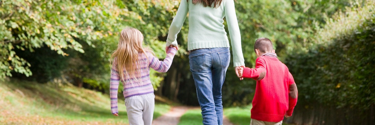 mother and two children walking on woodland path in autumn