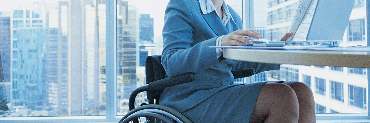 Businesswoman sitting in a wheelchair working on a laptop in the office.