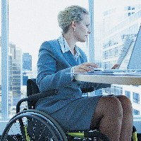 Businesswoman sitting in a wheelchair working on a laptop in the office.