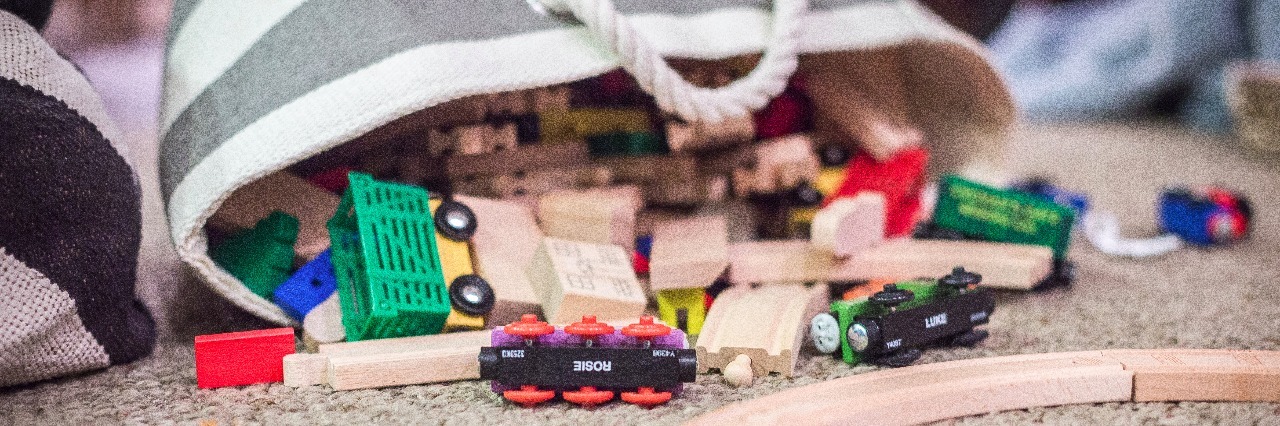 Bag full of children's toys laying on the floor with toys spilling out.