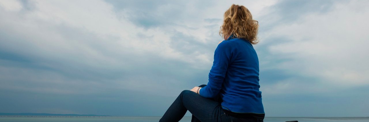 Woman With an Invisible Illness Hopes to Be More Understanding pensive woman sitting on the beach