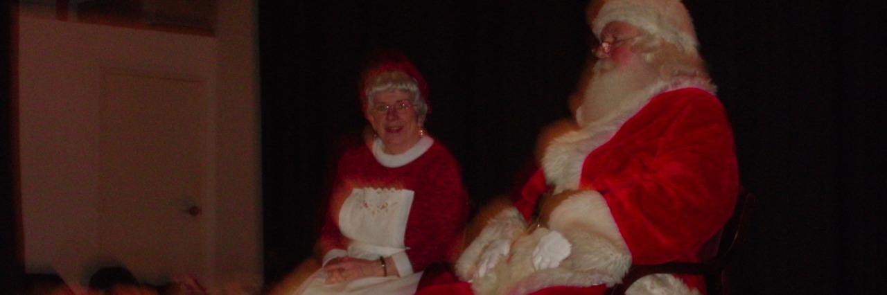 Santa Claus and Mrs. Clause sitting on a stage