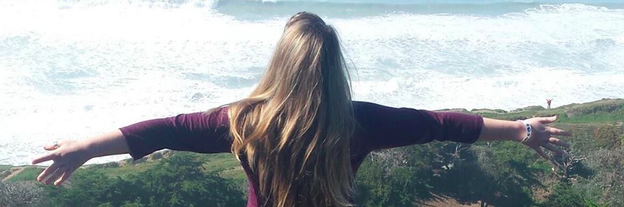 girl standing on cliff overlooking ocean with her arms outstretched