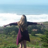 girl standing on cliff overlooking ocean with her arms outstretched
