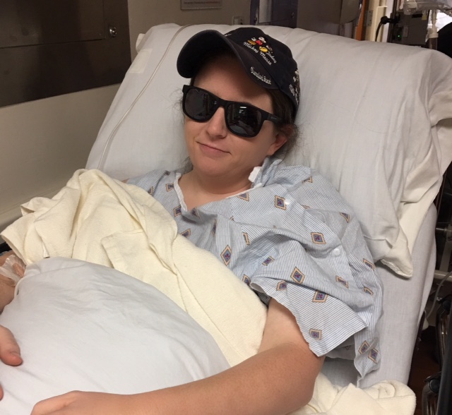 woman in a hospital bed wearing a baseball cap and sunglasses