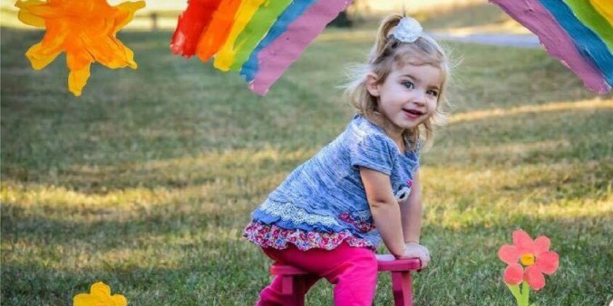 picture of young girl playing on grass field with rainbow drawn on the photo
