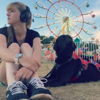 The author and her service dog sitting on the grass in front of a ferris wheel