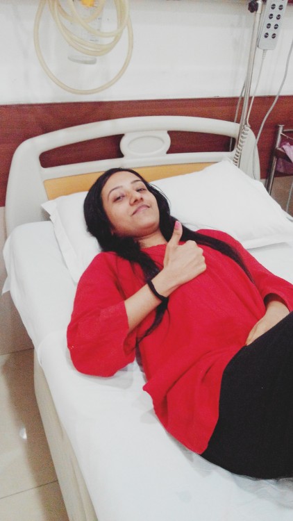 woman lying in hospital bed giving thumbs up sign