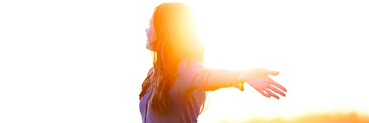 Choosing Simple Goals for 2017 as a Person With a Chronic Illness woman raising her arms in a field