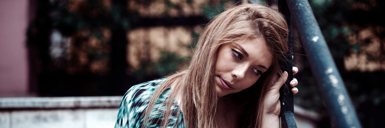 Depressed young adult sitting lonely outdoors and feeling so alone