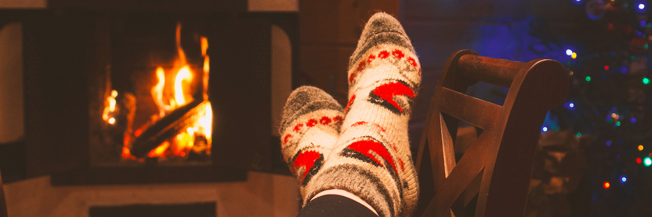 Tips for Getting Through Christmas With Depression and Anxiety woman is warming her legs near the fireplace in winter socks during the cristmas holidays