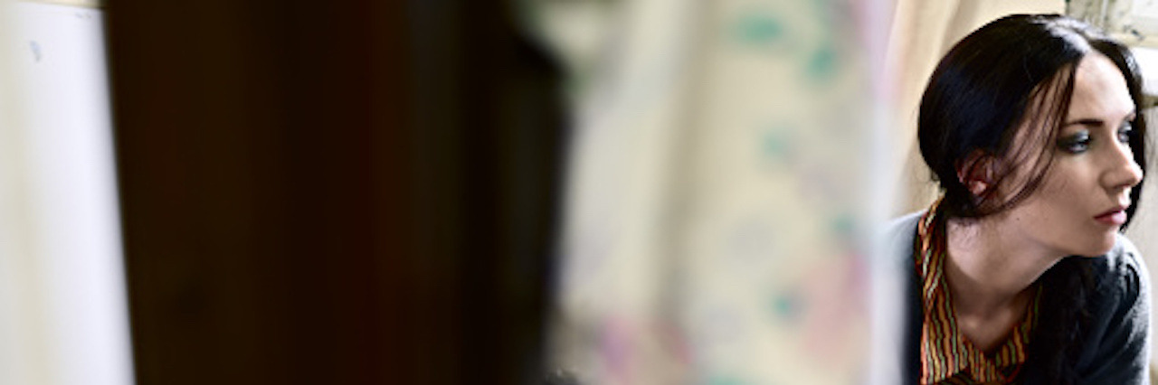 Letter to People Who Are Worried About Their Weight A sad young woman looking off to the side with a curtain to the left of her