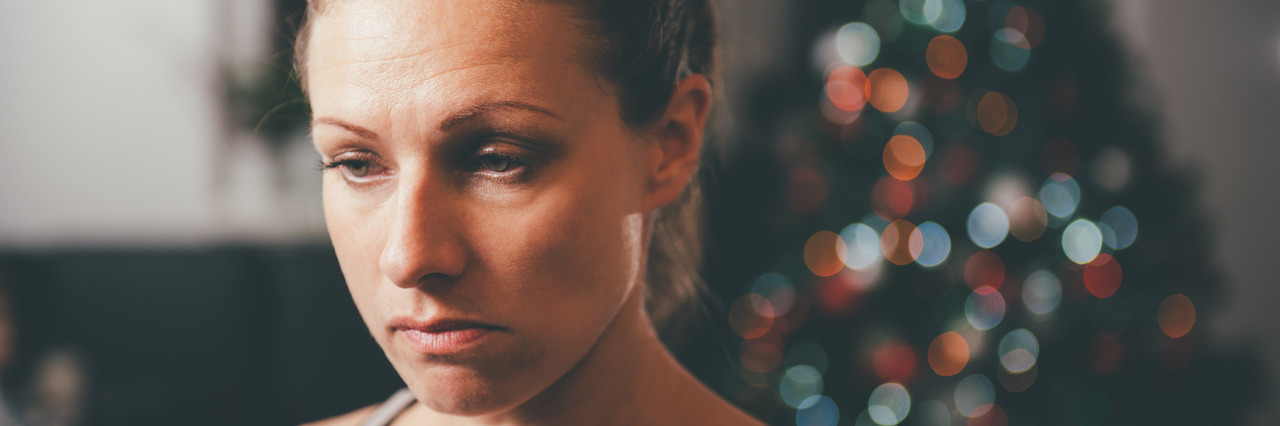 What It's Like to Have Depression at Christmastime Sad woman by the christmas tree contemplating