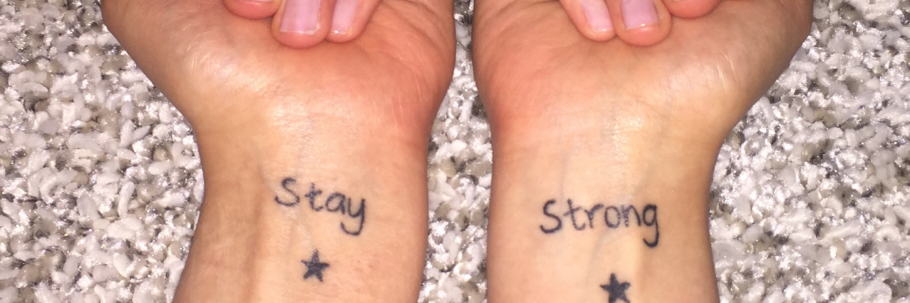 28 Tattoos That Cover Self-Harm Scars Someone holding out their wrists. One says "Stay" the other says "strong"