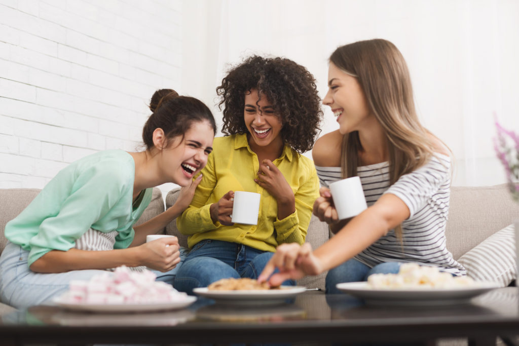 Image of three women laughing while drinking tea and eating snacks