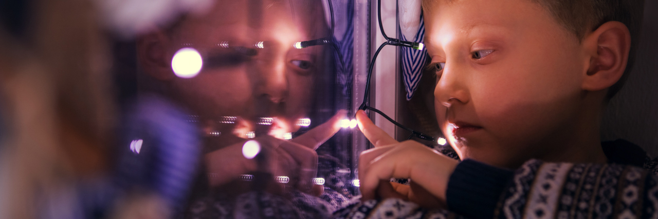 young boy sitting next to window fairy lights