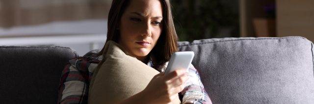 woman sitting on her couch and anxiously looking at her phone