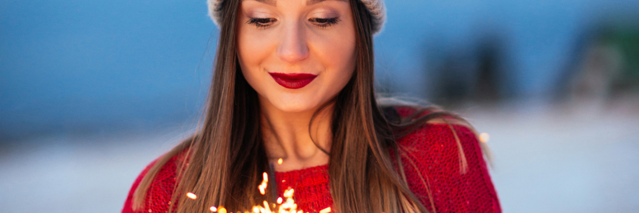 I'm Giving Up New Year's Resolutions for My Health A woman outside in the snow with a sparkler.