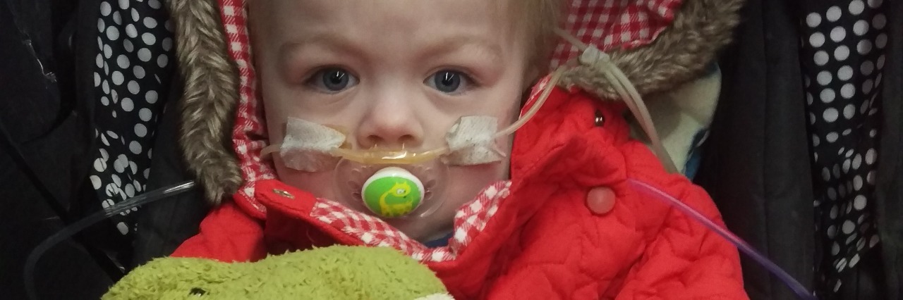 What Parents of Children With Rare Diseases Should Know author's son sitting in a stroller, wearing a red jacket and holding a green dinosaur stuffed animal