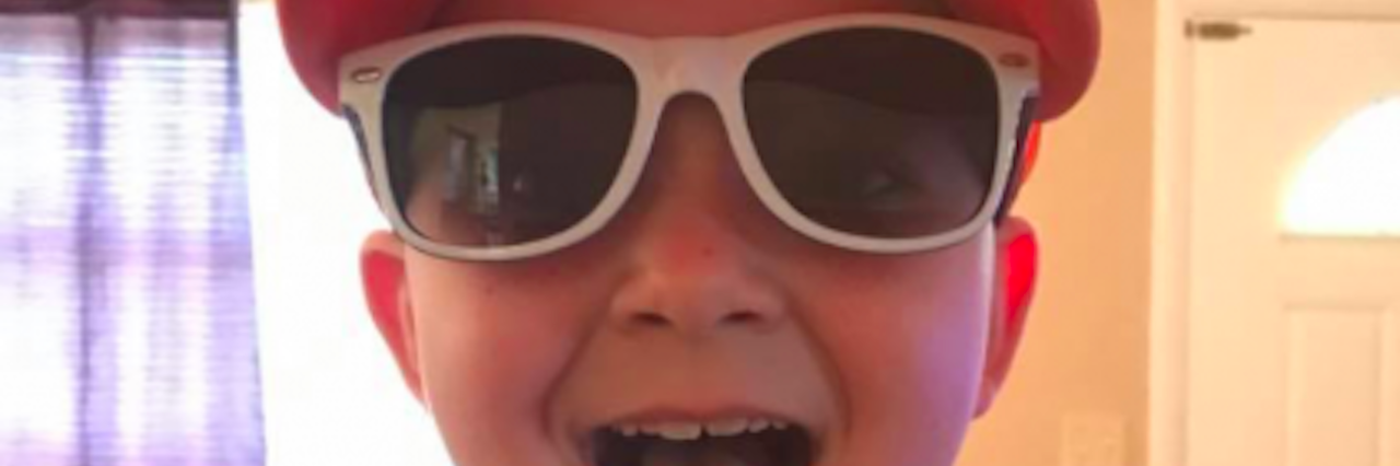 young boy in hat and sunglasses sticking his tongue out at the camera