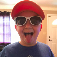 young boy in hat and sunglasses sticking his tongue out at the camera
