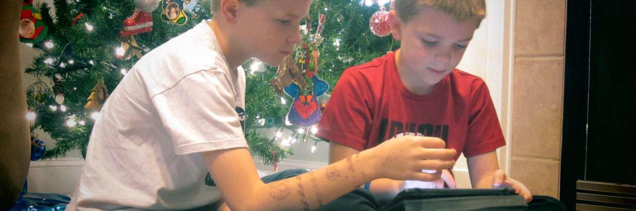 Children using a tablet by the Christmas tree.