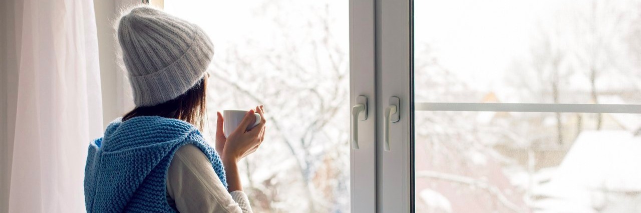 New Year’s Resolutions Are a Different Story for the Chronically Ill woman in a white hat and blue vest looking out a window on a winter's day