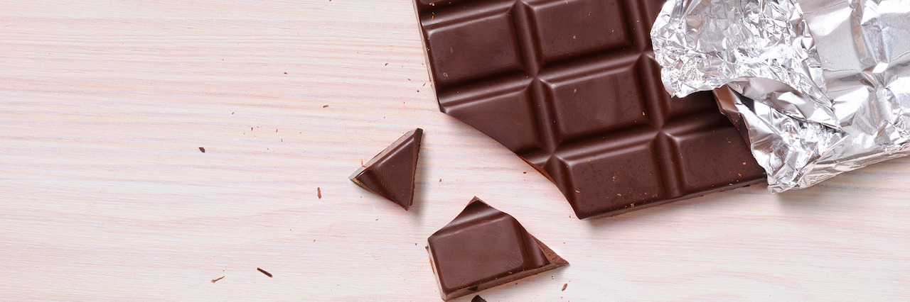 Detail of chocolate bar with silver wrapping on a wooden table with a broken portion. Horizontal composition. Top view