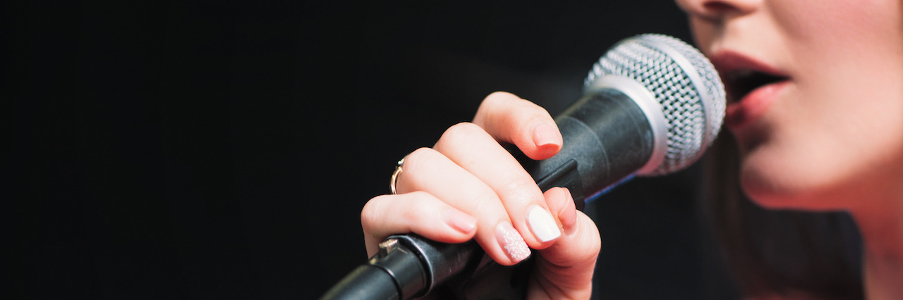 How Writing and Spoken Word Help When Coping With PTSD Microphone and unrecognizable female singer close up. Cropped image of female singer in pink dress , singing into a microphone, holding mic with two hands.