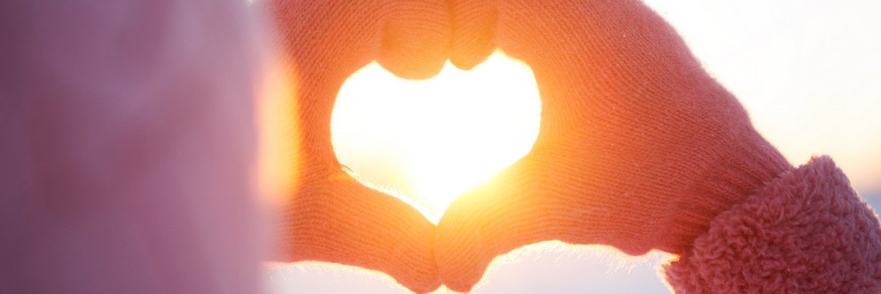 woman makes a heart symbol with her hands in during winter