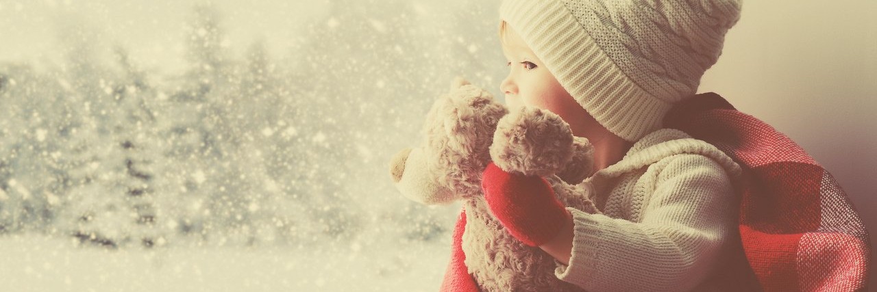 little girl with teddy bear looking out a window during winter