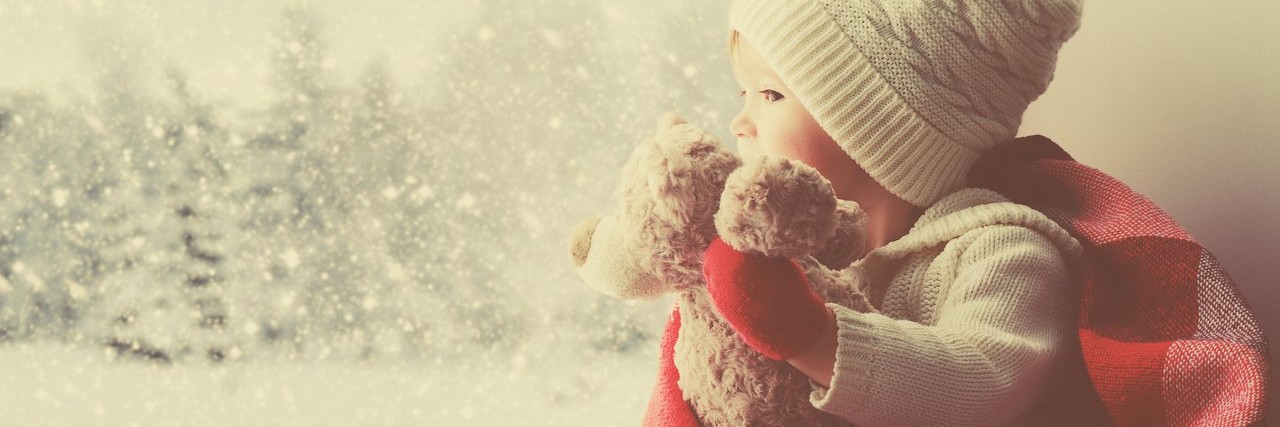 Things Parents of Children With Rare Diseases Want for Christmas little girl with teddy bear looking out a window during winter