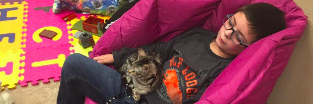 Purrs for Autism Pairs Kids With Autism With Kittens for Social Play Young boy laying on a beanbag a kitten on a leash is sitting in his lap