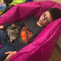 Young boy laying on a beanbag a kitten on a leash is sitting in his lap