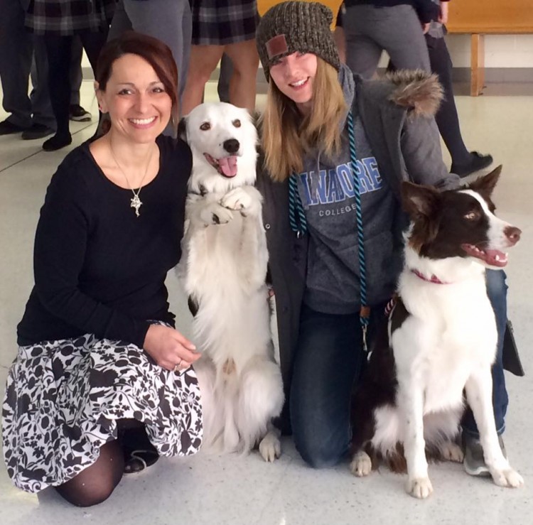 teacher smiles with former student and two dogs