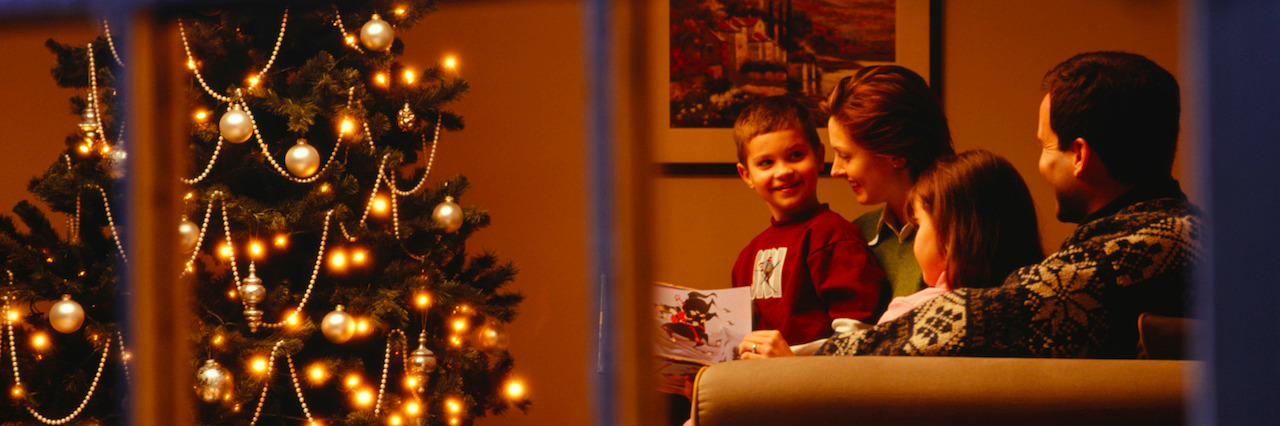 Family reading together on sofa at Christmas time, viewed through window