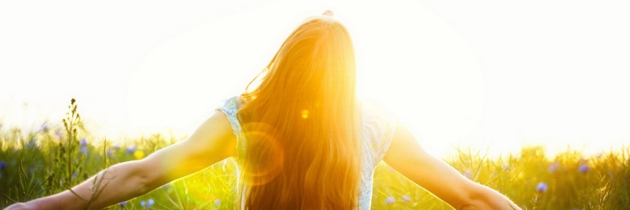 Quotes That Give Me Strength as a Person With a Chronic Illness young woman enjoying sunlight with raised arms in canola field